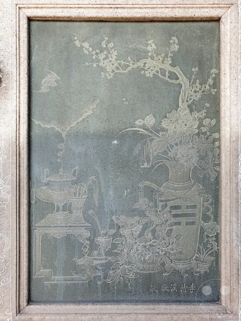 Ein kunstvolles Steinrelief im Mengjia Longshan Tempel in Taipeh, Taiwan, zeigt eine traditionelle chinesische Szenerie mit Blumen, Vasen und archaischen Gefäßen. Die feine Gravur auf dem dunklen Stein vermittelt eine Atmosphäre von Ruhe und historischer Bedeutung. Dieses Kunstwerk spiegelt die reiche kulturelle Erbschaft und die kunsthandwerkliche Tradition Taiwans wider.