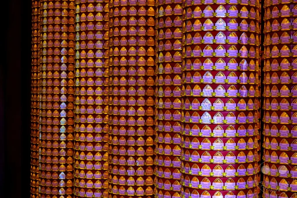 Eine Wand voller tausender kleiner, orangefarbener Gebetslichter im Mengjia Longshan Tempel in Taipeh, Taiwan. Die Lichter sind in geometrischen Reihen angeordnet und erzeugen ein warmes, atmosphärisches Lichtspiel. Die Szene strahlt eine tiefe Ruhe und Spiritualität aus, typisch für buddhistische Tempel.