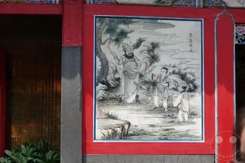 Eine traditionelle chinesische Malerei ziert eine rote Säule des Mengjia Longshan Tempels in Taipeh, Taiwan. Sie stellt eine Szene mit mehreren Figuren dar, darunter ein Krieger mit Bart, ein Kind mit einem Tier und eine weitere Person. Die gedämpften Farben und der stilisierte Pinselstrich vermitteln eine Atmosphäre von Geschichte und spiritueller Bedeutung im Herzen der Stadt.