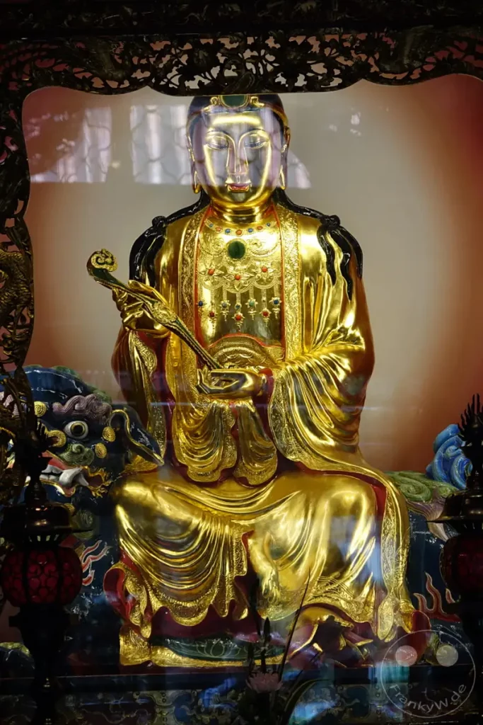 Eine goldene Buddha-Statue sitzt in einer prächtigen Haltung im Mengjia Longshan Tempel in Taipeh, Taiwan. Der detailreich verzierte Sitz und die Kleidung der Figur spiegeln die kunstvolle Handwerkskunst wider, während die meditative Ausstrahlung Ruhe und Ehrfurcht vermittelt. Das Lichtspiel auf der vergoldeten Oberfläche unterstreicht die spirituelle Atmosphäre des heiligen Ortes.