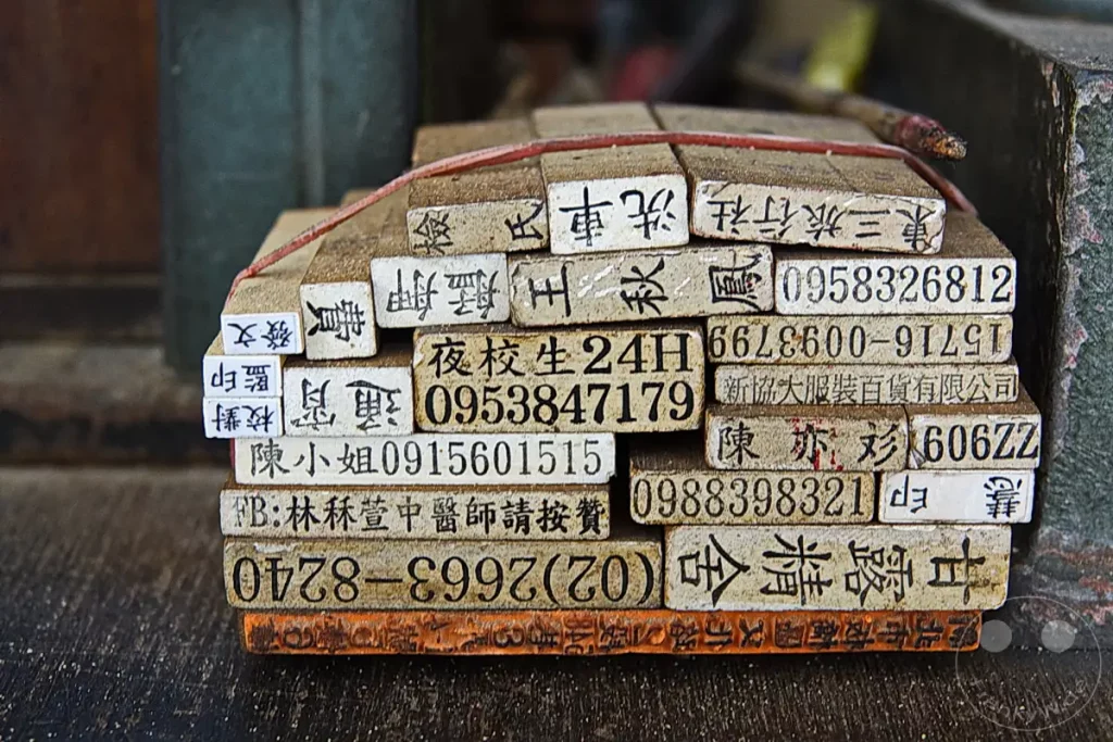 Gestapelte Holzstempel mit chinesischen Schriftzeichen und Zahlen sind auf einem Holztisch in Taipeh, Taiwan, arrangiert. Die groben Holzblöcke und die verblassten Zeichen deuten auf ein traditionelles Handwerk hin, das von der Zeit gezeichnet ist. Die Szene vermittelt ein Gefühl von Nostalgie und der Beständigkeit alter Handwerkstechniken.