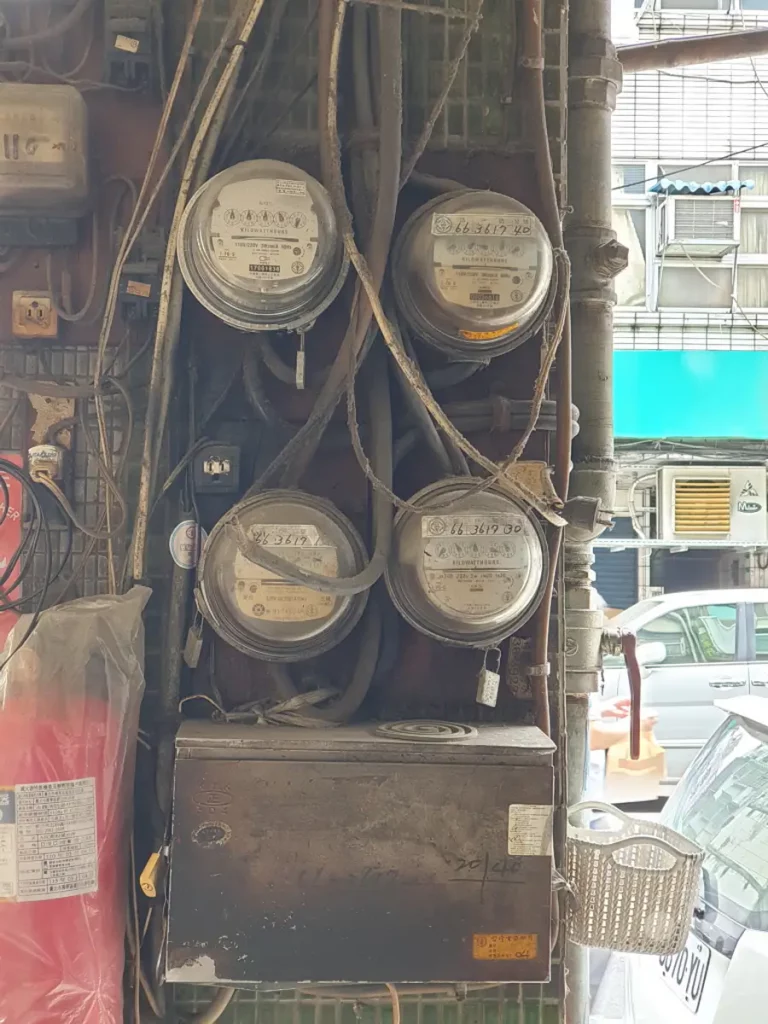 In Taipeh, Taiwan, ist eine veraltete Stromversorgung mit mehreren Stromzählern und dicht verlegten Kabeln zu sehen. Die Szene vermittelt einen Eindruck von städtischer Infrastruktur und der Organisation der Energieverteilung. Helle und dunkle Bereiche sowie die Struktur der Meter und Kabel dominieren das Bild.
