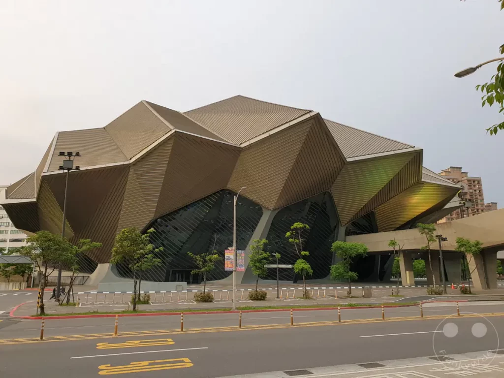 Das Taipei Music Center in Taiwan besticht durch seine futuristische und skulpturale Architektur, die an natürliche Formen erinnert. Die goldbraune Fassade des Gebäudes reflektiert das Licht und harmoniert mit den umliegenden Grünflächen und dem bedeckten Himmel. Eine ruhige und beeindruckende Atmosphäre strahlt das Zentrum aus, das sich in das Stadtbild von Taipeh einfügt.