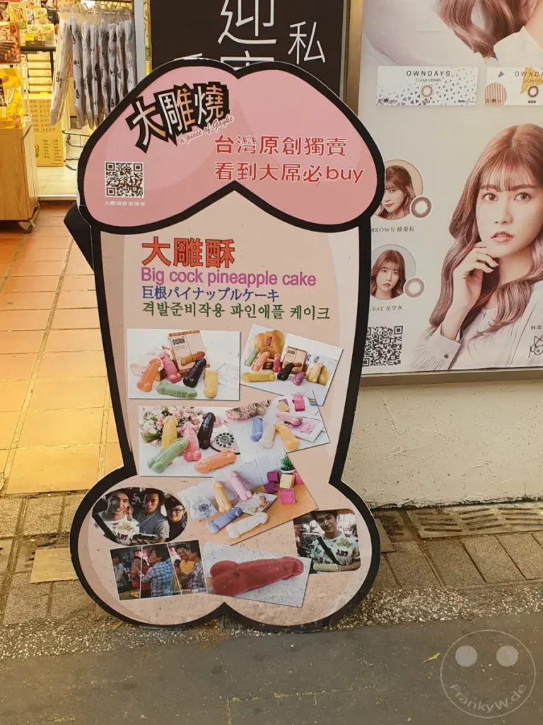 In Taipeh, Taiwan, steht vor einem Geschäft in Xinmen ein aufsehenerregendes Werbeschild in Form eines Penis, das für "Big cock pineapple cake" wirbt. Die farbenfrohe Gestaltung und die humorvolle Aufmachung ziehen die Aufmerksamkeit von Passanten auf sich. Mehrere Fotos von den originell geformten Kuchen und glücklichen Kunden runden das ungewöhnliche Werbekonzept ab.