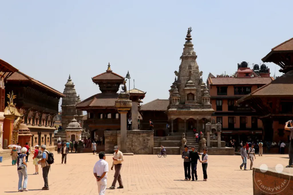 Ein sonniger Tag auf dem Platz von Bhaktapur, Nepal, umgeben von traditioneller Architektur. Menschen schlendern über den gepflasterten Boden und bewundern die Tempel und Gebäude.