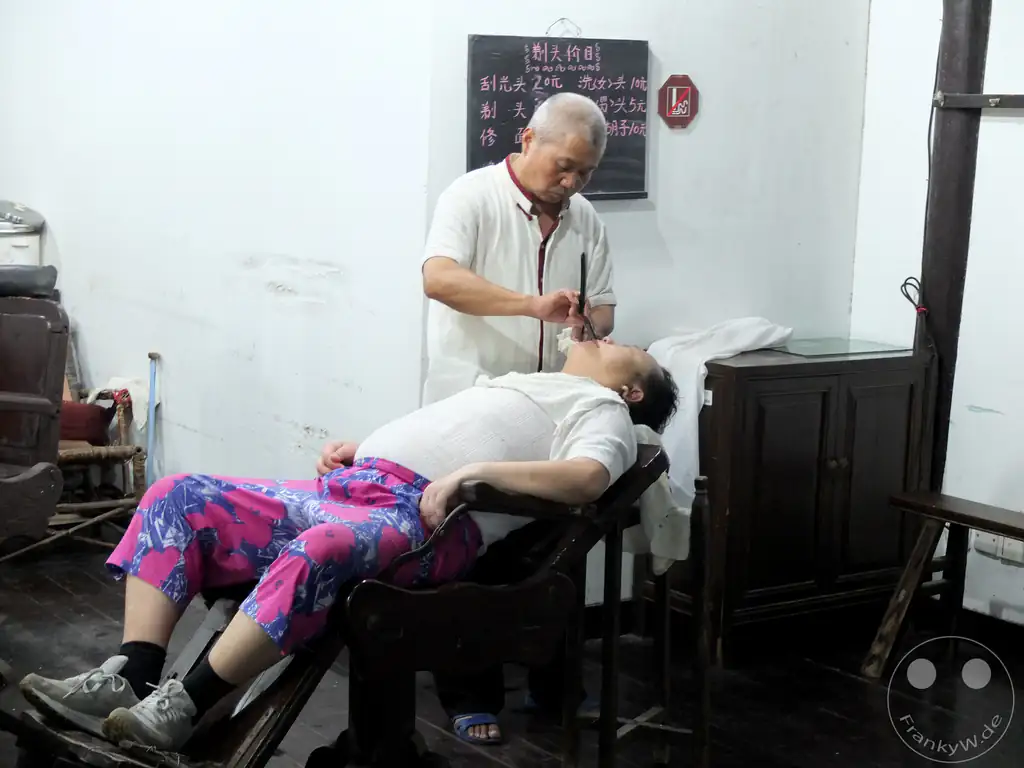 China - Wuzhen - A barber shaves a customer in a traditional wooden chair