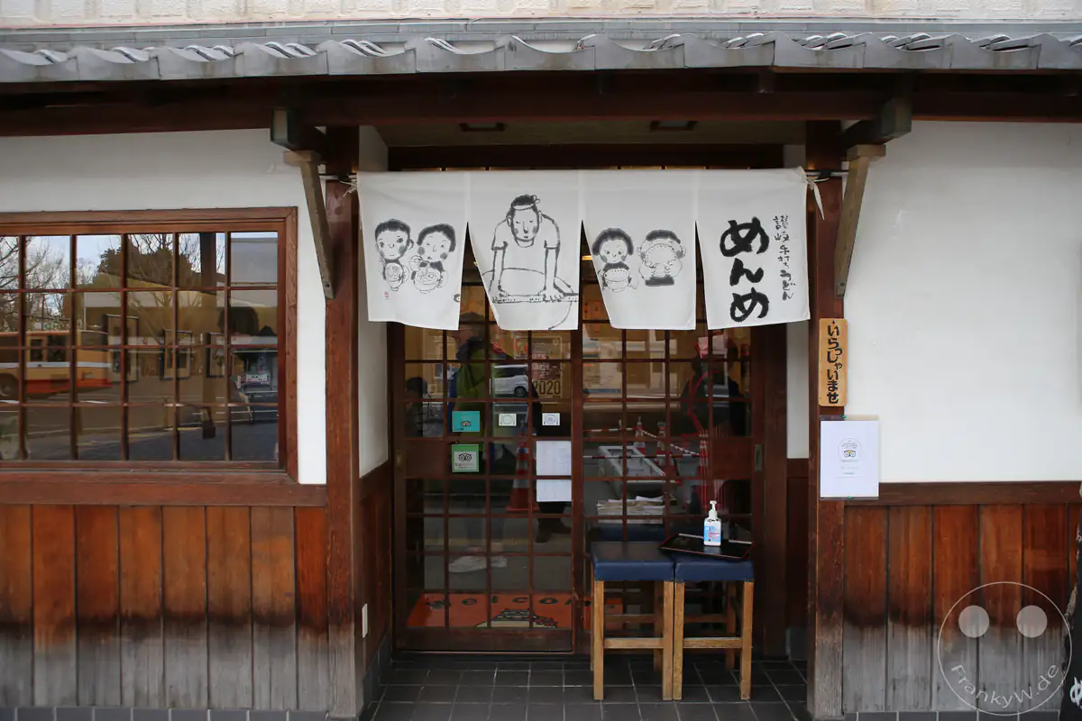 Der traditionelle Eingang eines japanischen Restaurants in Himeji ist mit einem weißen Noren-Vorhang dekoriert, der kunstvolle handgezeichnete Skizzen von Gesichtern und Schriftzeichen zeigt