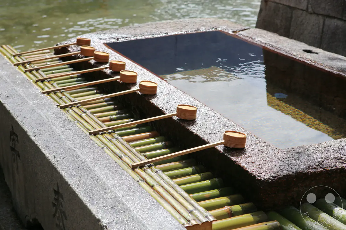 Traditionelle hölzerne Schöpfkellen liegen ordentlich aufgereiht an einem steinernen Chozuya-Reinigungsbecken für rituelle Waschungen vor dem Besuch eines japanischen Shinto-Schreins.