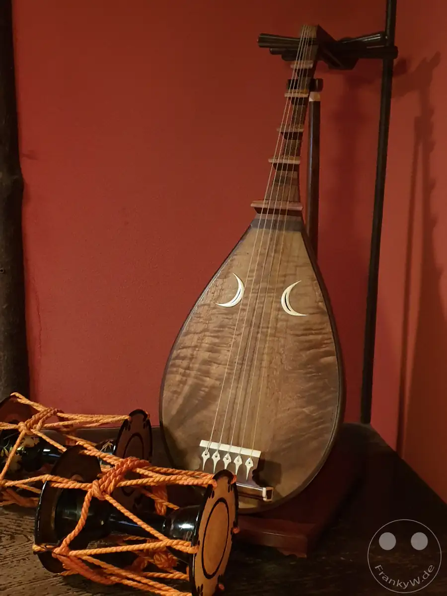 Traditionelle japanische Biwa-Kurzhalslaute mit sichelförmigen Schalllöchern und eine kunstvoll geschnürte Tsuzumi-Handtrommel vor einer roten Wand im historischen Shima-Teehaus in Kanazawa, Japan.