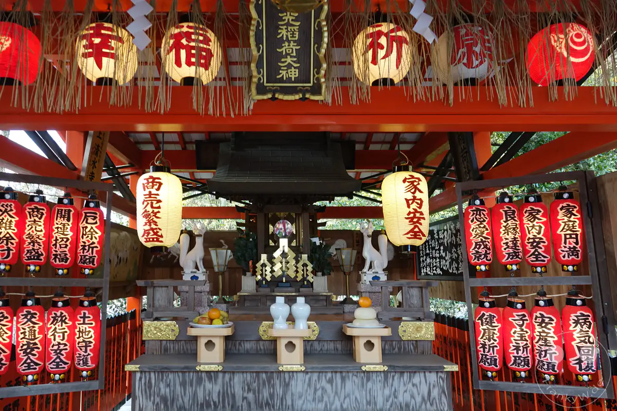 Ein prachtvoller Shinto-Altar, der dem Inari-Kult gewidmet ist, geschmückt mit traditionellen Papierlaternen, rituellen Opfergaben auf Holztischen und zwei weißen Kitsune-Fuchsfiguren.