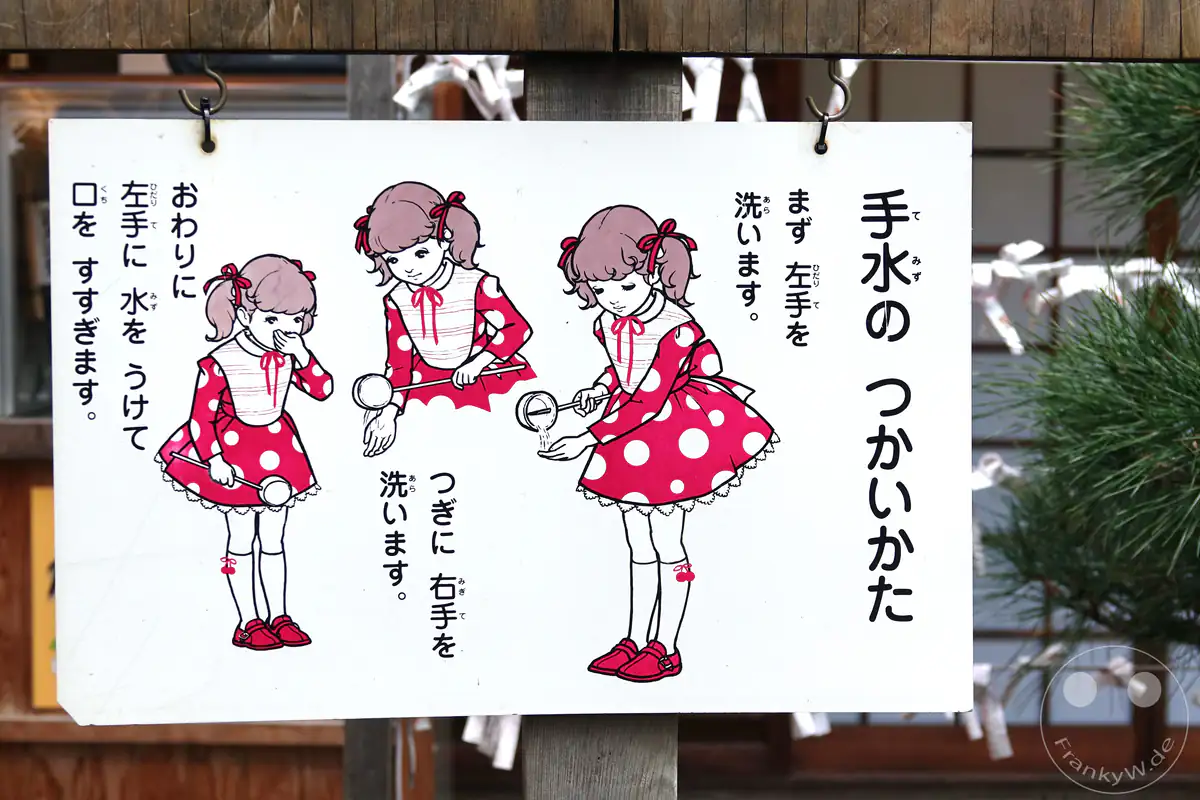 Ein illustriertes Hinweisschild an einem japanischen Shinto-Schrein erklärt mit einer kindgerechten Comicfigur Schritt für Schritt die traditionelle rituelle Reinigung der Hände und des Mundes.