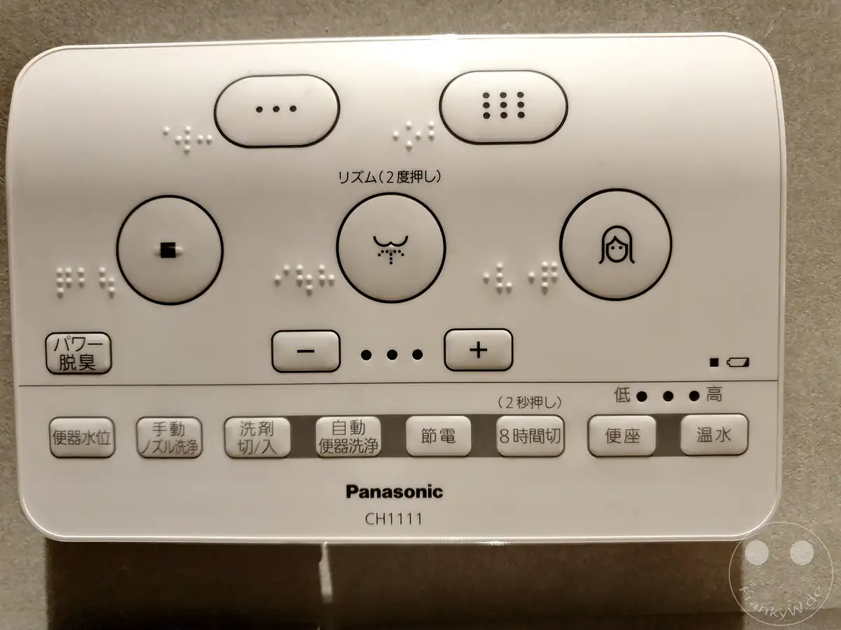 Eine wandmontierte elektronische Panasonic CH1111 Fernbedienung für ein modernes japanisches Dusch-WC mit zahlreichen Funktionstasten, Brailleschrift und japanischen Schriftzeichen.