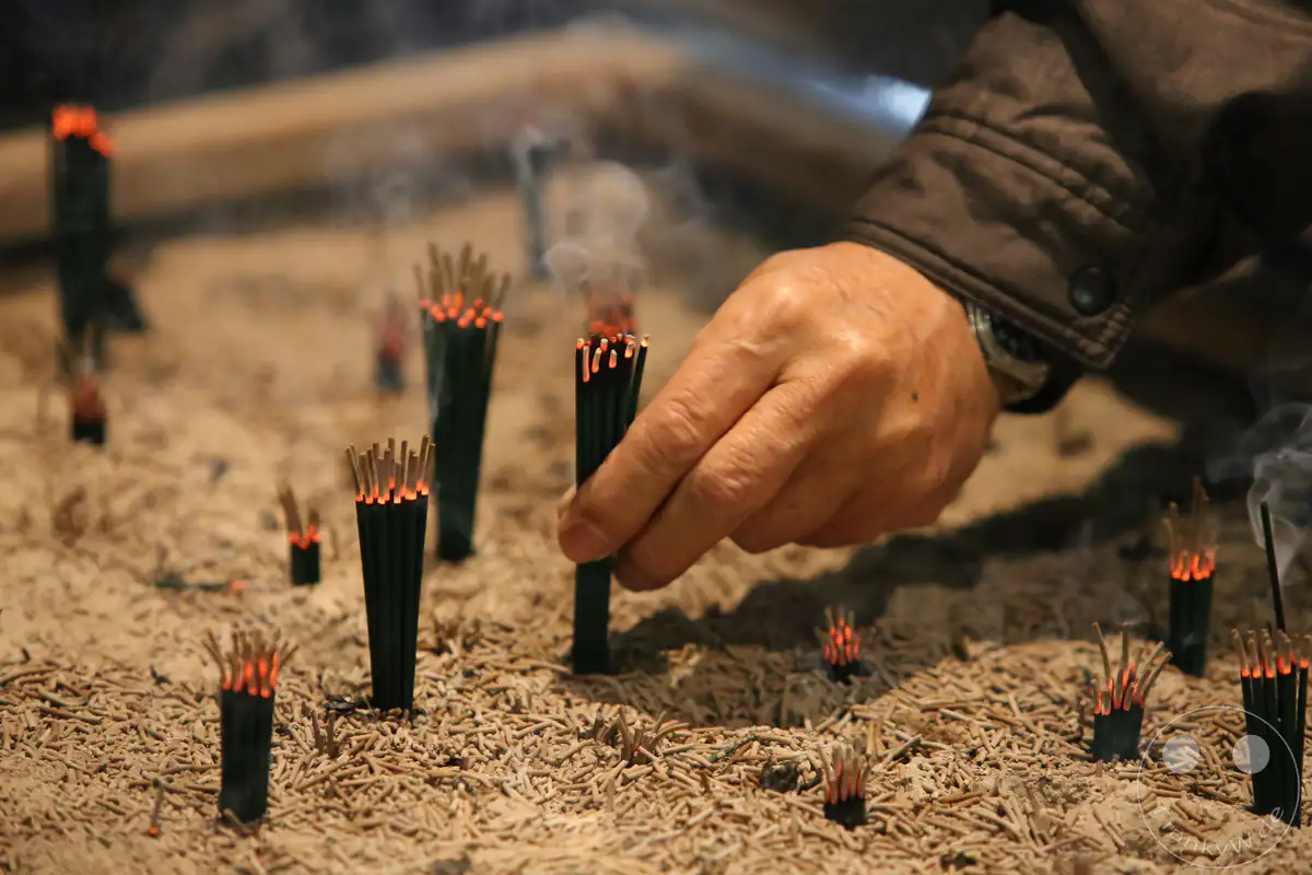 Die Hand eines gläubigen Besuchers platziert glimmende schwarze Räucherstäbchen in einem großen, mit Asche gefüllten Becken während des historischen Hadaka-Matsuri-Festivals am Saidai-ji Kannon-in Tempel in Okayama.