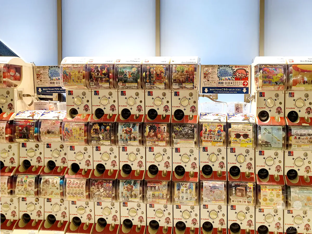 Eine lange, mehrstöckige Reihe von weißen Gashapon-Spielzeugautomaten mit bunten Schaukästen für verschiedene Anime-Sammelfiguren wie Dragon Ball und Mario in einer Filiale von Bic Camera im Stadtteil Chiyoda in Tokio, Japan.