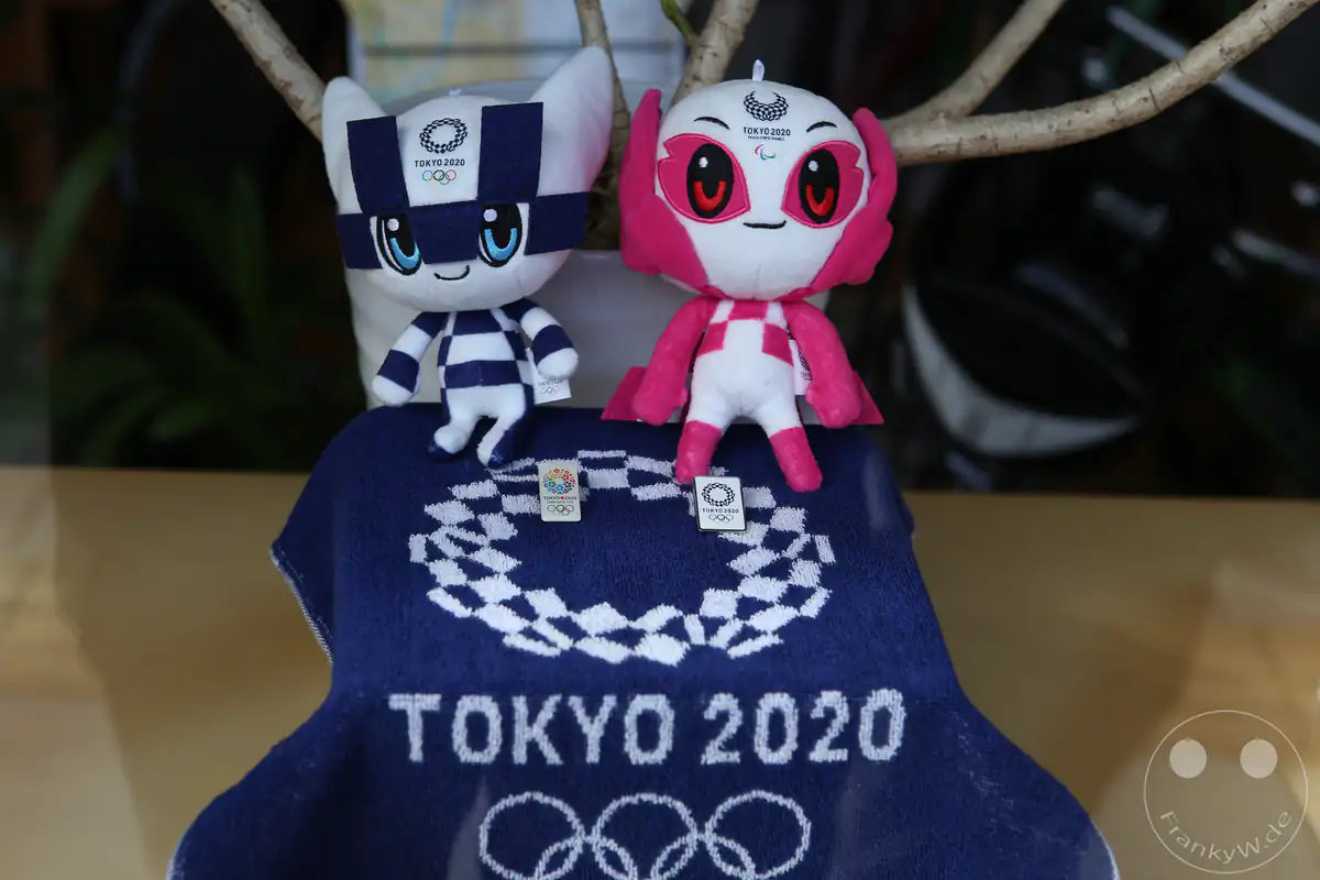 Die offiziellen Plüsch-Maskottchen Miraitowa und Someity der Olympischen und Paralympischen Spiele von Tokio 2020 sitzen dekorativ auf einem dunkelblauen Fan-Handtuch mit dem gestickten Logo und den olympischen Ringen in Japan.