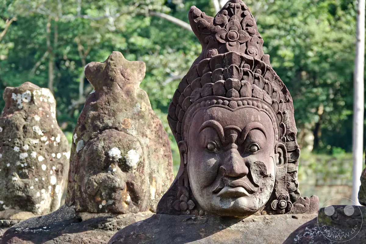Nahaufnahme einer steinernen Dämonenstatue (Asura) mit grimmigem Gesichtsausdruck und verziertem Kopfschmuck am Südtor von Angkor Thom in Kambodscha.