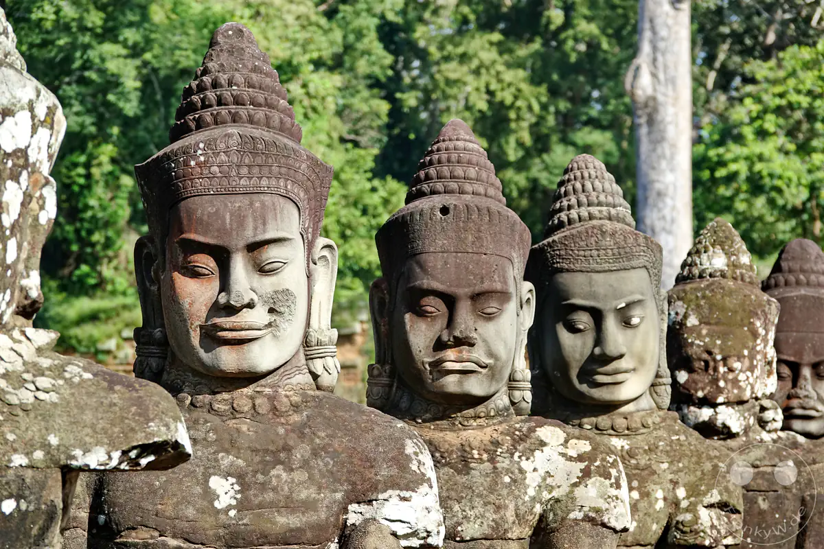 Nahaufnahme von steinernen Götterstatuen (Devas) mit traditionellem Kopfschmuck auf der Brücke vor dem Südtor von Angkor Thom in Kambodscha.