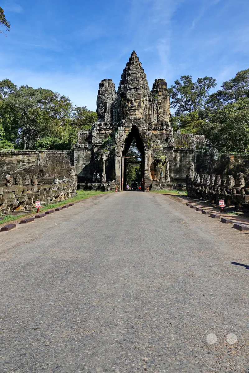 Das historische Südtor der antiken Khmer-Stadt Angkor Thom in Kambodscha mit der von Steinstatuen gesäumten Brücke und den monumentalen Gesichtern auf dem Torbogen.