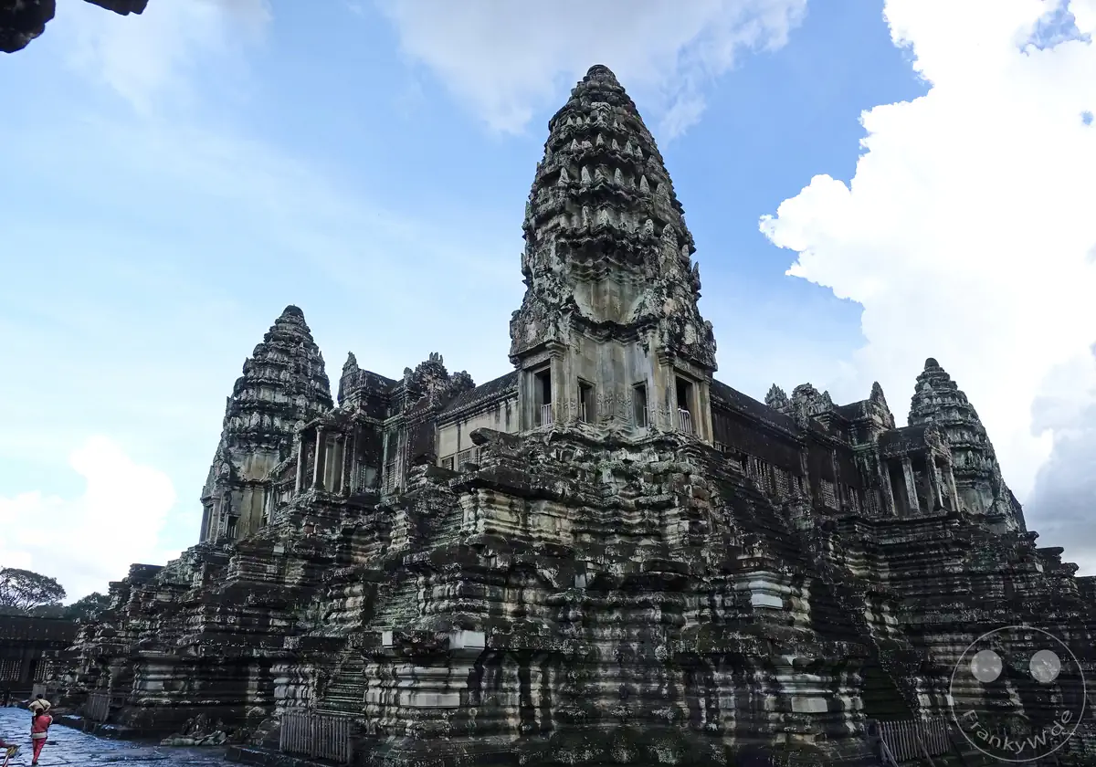 Die monumentale Ansicht der historischen, pyramidenförmig aufgebauten Steintürme von Angkor Wat, die sich über den terrassenförmigen Ebenen der Tempelanlage gegen einen leicht bewölkten, blauen Himmel erheben.