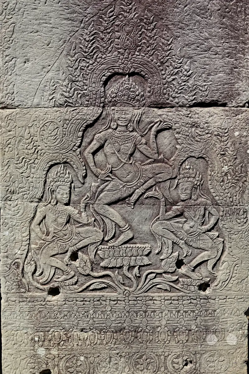 Ein detailreiches, historisches Steinrelief an einer Tempelmauer in Angkor mit der Darstellung von tanzenden Apsara-Himmlerinnen auf Lotusblüten.
