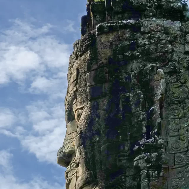 Seitenprofil eines monumentalen, in den Stein gemeißelten Gesichts im Bayon-Stil auf dem historischen Südtor der antiken Stadt Angkor Thom in Kambodscha vor blauem Himmel.