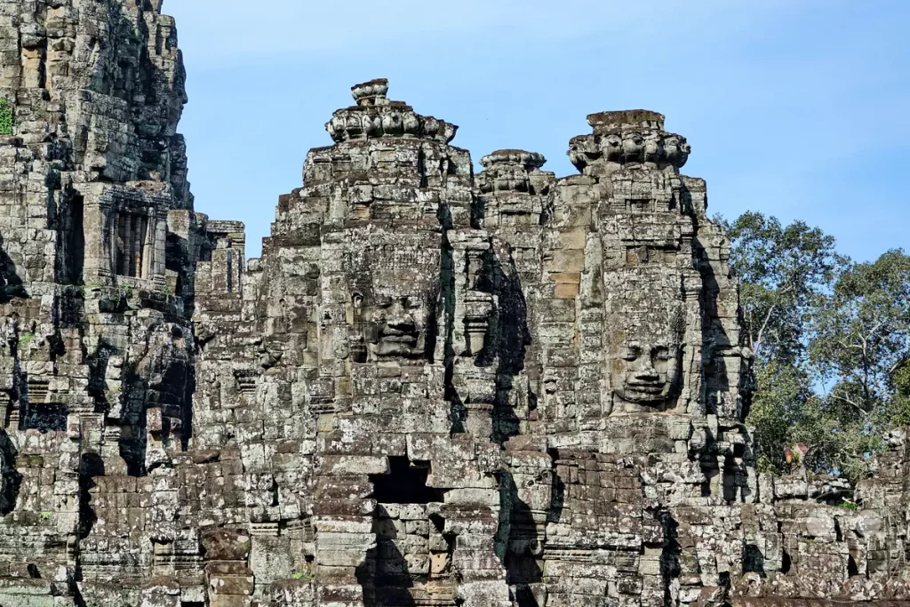 Die monumentalen, in den Stein gemeißelten Gesichter auf den Türmen des historischen Bayon-Tempels in Angkor Thom, Kambodscha, vor einem hellen Himmel.