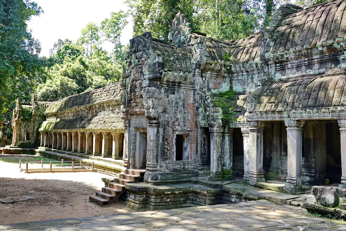 Die weitläufige historische Fassade des Preah-Khan-Tempels in Angkor mit einem markanten steinernen Treppenaufgang, kunstvoll verzierten Toren und langen, von Säulen getragenen Galeriegängen vor grünem Wald.