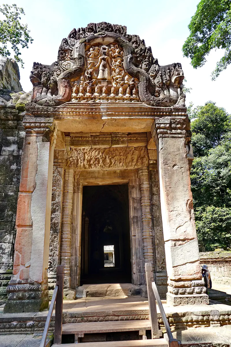 Historischer Steineingang (Gopuram) der Ta-Prohm-Tempelanlage in Angkor. Der monumentale Torbogen ist mit feinen Khmer-Sandsteinreliefs verziert und führt in einen dunklen Gang, umgeben von dichtem, grünem Dschungel.