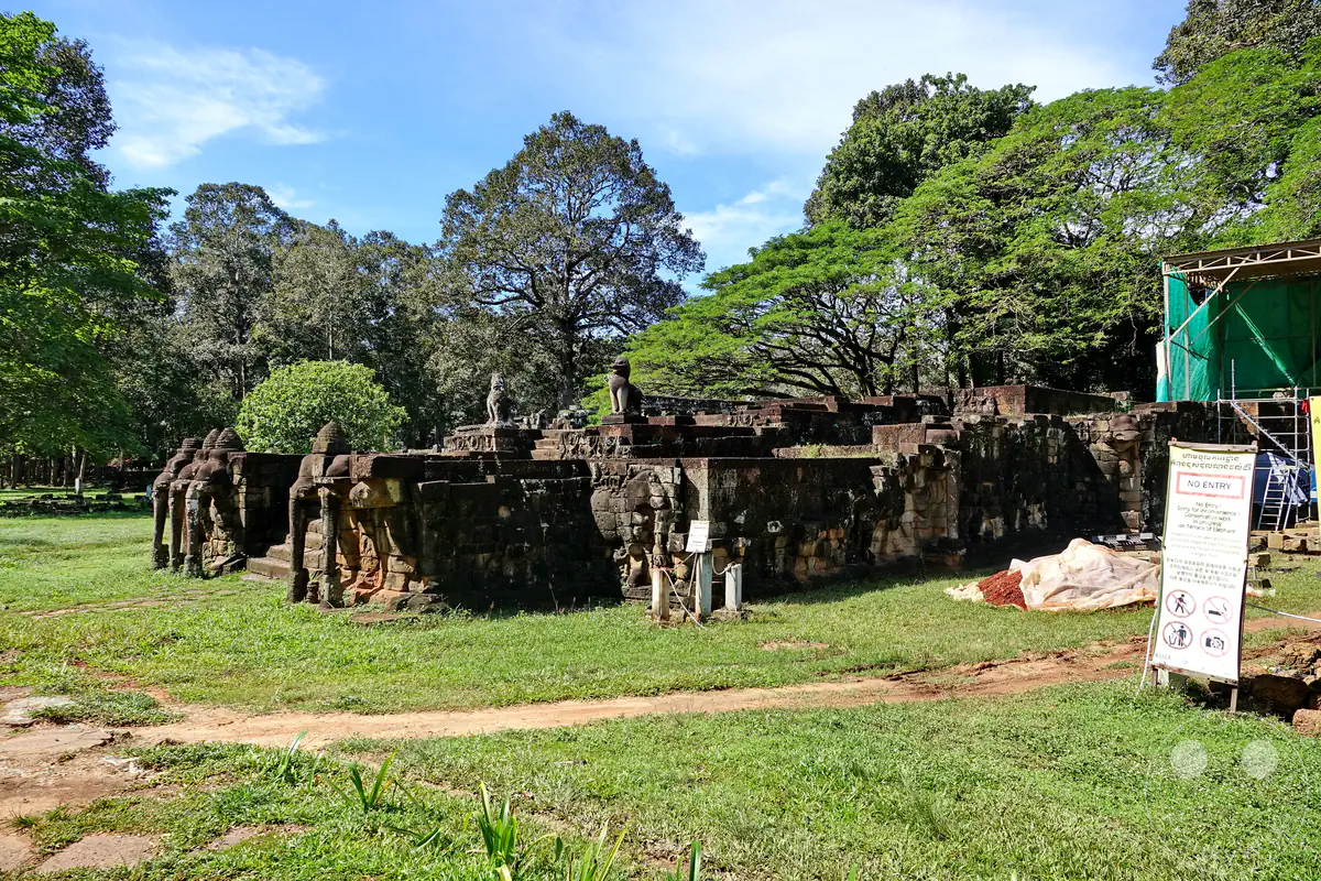 Die historische Terrasse der Elefanten in der antiken Stadt Angkor Thom mit ihren charakteristischen Steinelefanten an den Ecken, umgeben von grünen Rasenflächen und dichten Bäumen.