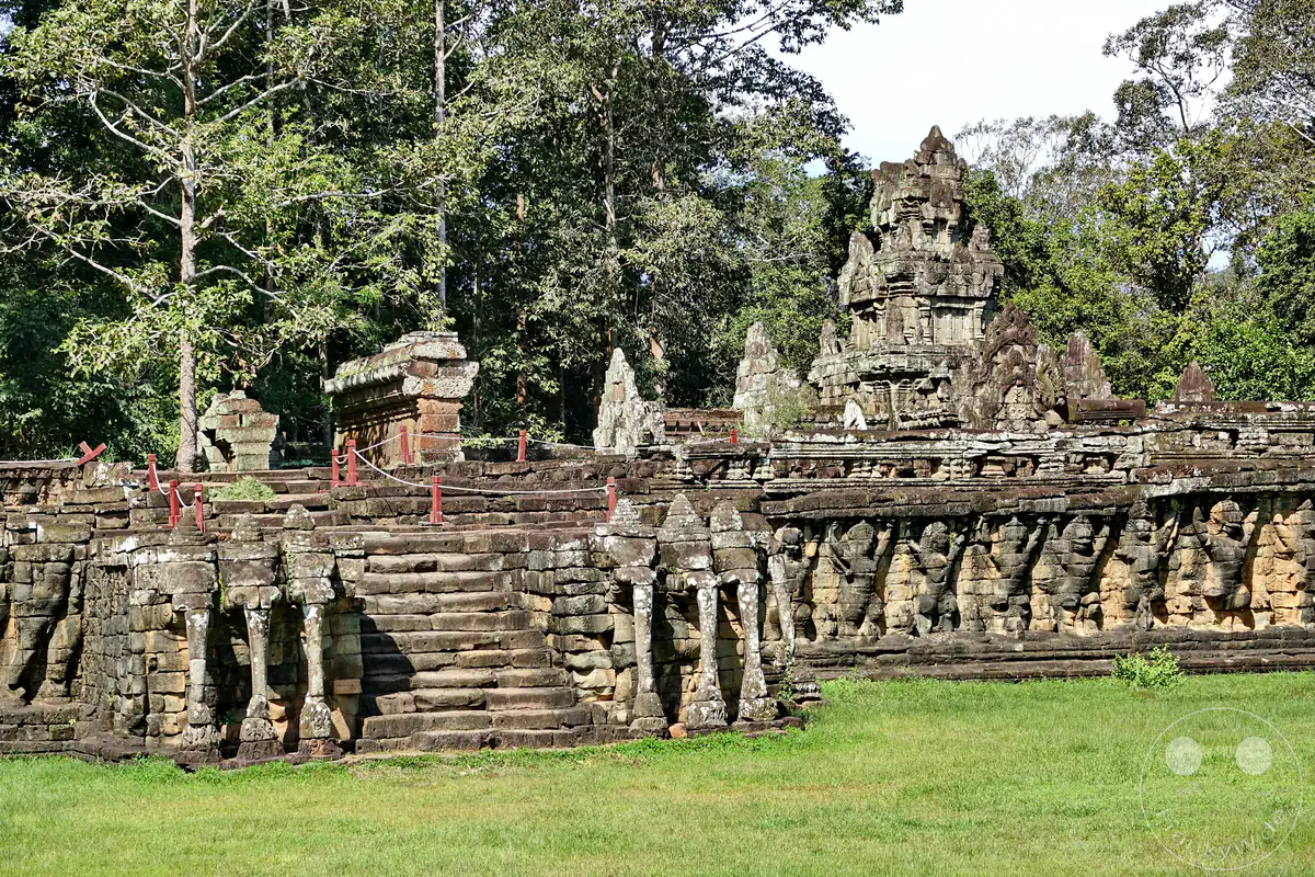 Ein historischer Treppenaufgang an der Terrasse der Elefanten in Angkor Thom mit den markanten dreiköpfigen Elefantenskulpturen, einer Reihe von Garuda-Reliefs und einem Steinturm im Hintergrund.
