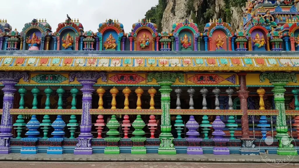 Frontalansicht einer detailreich verzierten, farbenprächtigen Balustrade und Fassade am Sri Subramaniar Swamy Tempel bei den Batu Caves nahe Kuala Lumpur, Malaysia, mit bunten Säulen, Mustern und einer Reihe kleiner hinduistischer Götterstatuen in Nischen an der Oberseite.