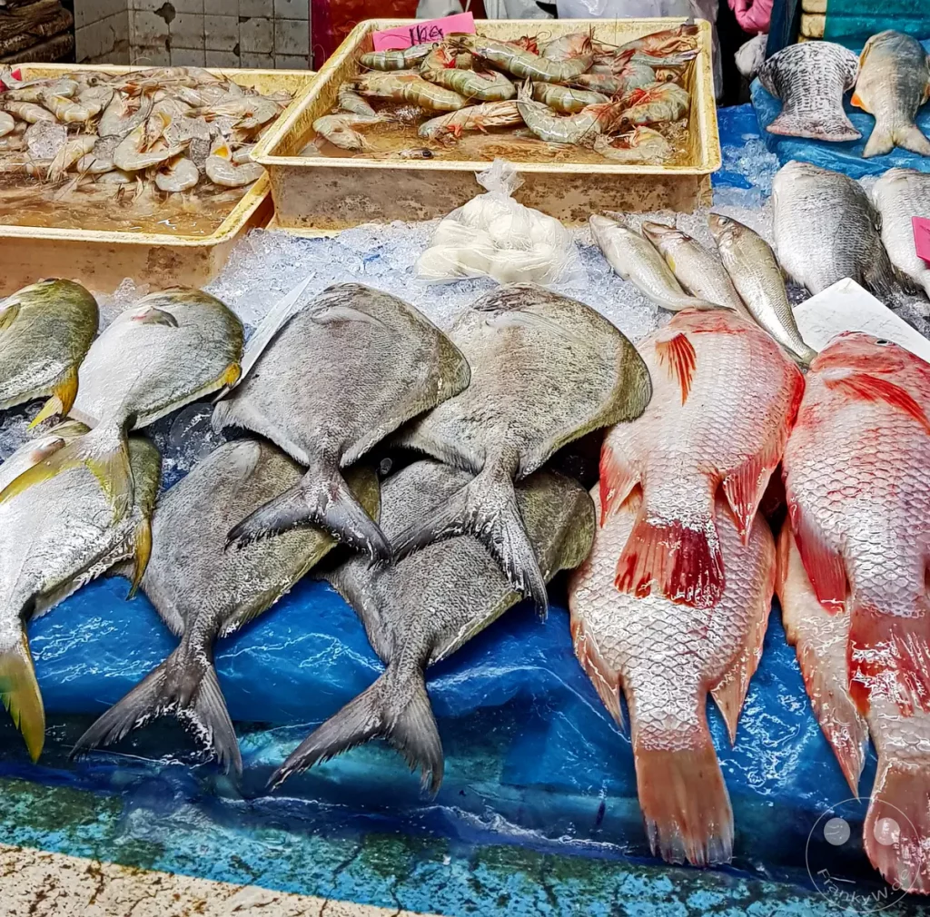 Frischer Fisch und Meeresfrüchte auf einer eisgekühlten blauen Plastikplane an einem Marktstand auf dem Pasar Besar Taman Tun Dr. Ismail in Kuala Lumpur, Malaysia, darunter roter Snapper, Pomfret-Fische sowie Kisten mit Garnelen im Hintergrund.