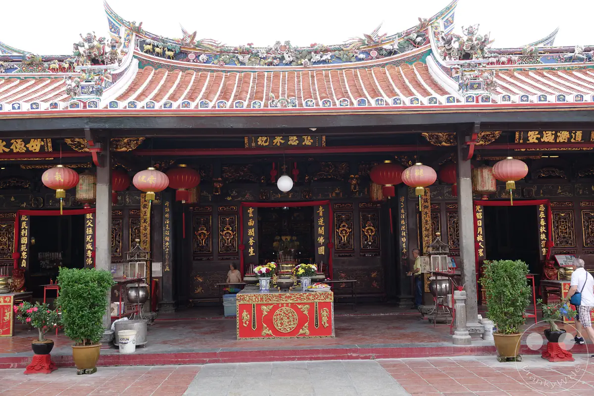 Der reich verzierte Eingangsbereich des historischen Cheng Hoon Teng Tempels in Malakka, Malaysia, mit traditionellen roten Lampions, vergoldeten Schriftzeichen auf schwarzen Holzsäulen, einem Opfertisch im Zentrum und kunstvollen Skulpturen auf dem geschwungenen Ziegeldach.