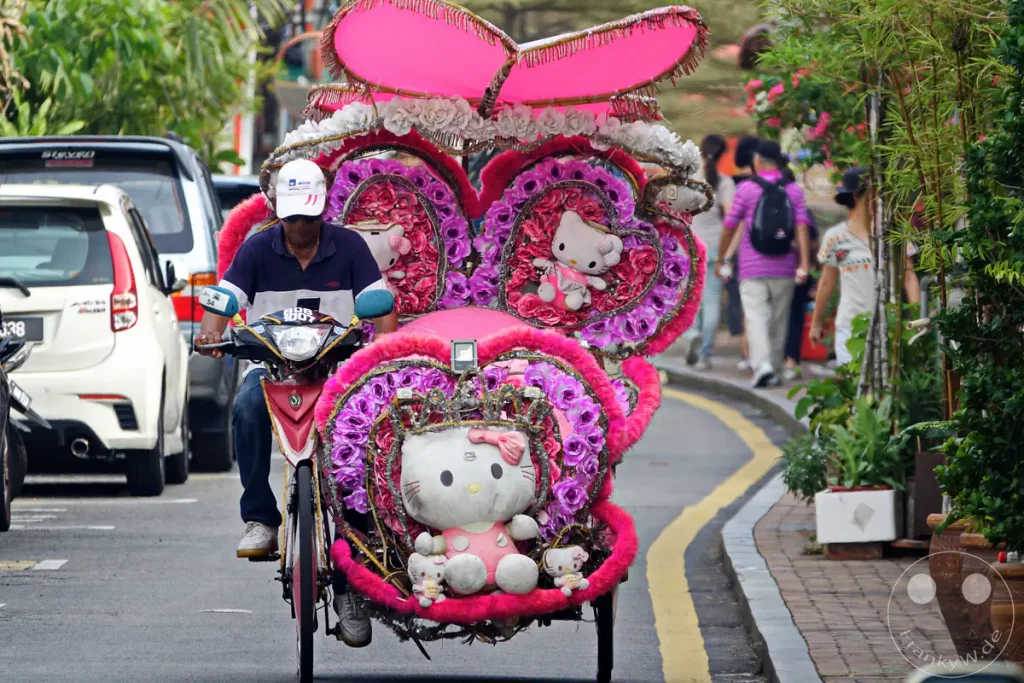 Fahrrad-Rikscha aufwändig und farbenfroh mit Hello-Kitty-Plüschfiguren, Lichterketten und künstlichen Blumen dekoriert in Malakka, Malaysia.