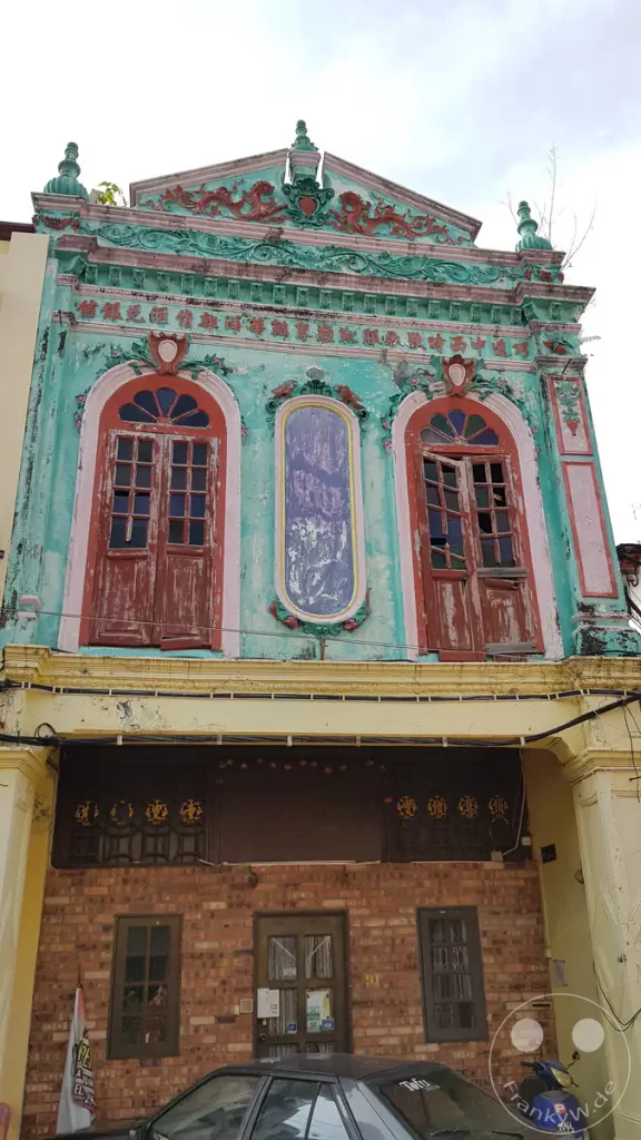 Fassade eines historischen, türkisfarbenen Peranakan-Shophouses im Kolonialstil mit verzierten Giebeln, hölzernen Fensterläden und traditionellen Schriftzeichen an der Tofu-Street in Malakka, Malaysia.