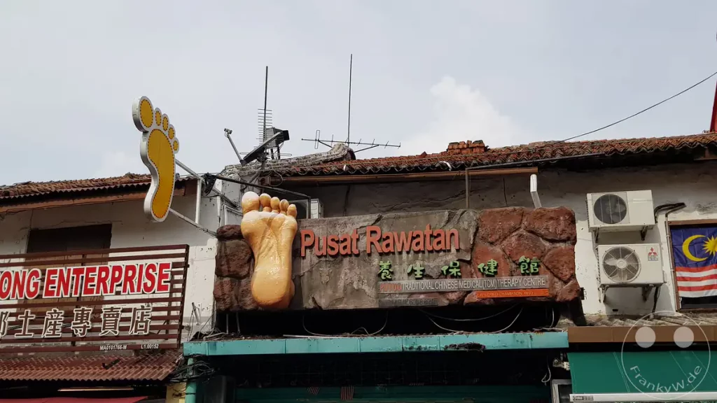 Ein auffälliges Werbeschild für ein Zentrum für Traditionelle Chinesische Medizin und Fußreflexzonenmassage (Pusat Rawatan) in der Stadt Melaka mit zwei großen plastischen Fuß-Symbolen über dem Eingang.