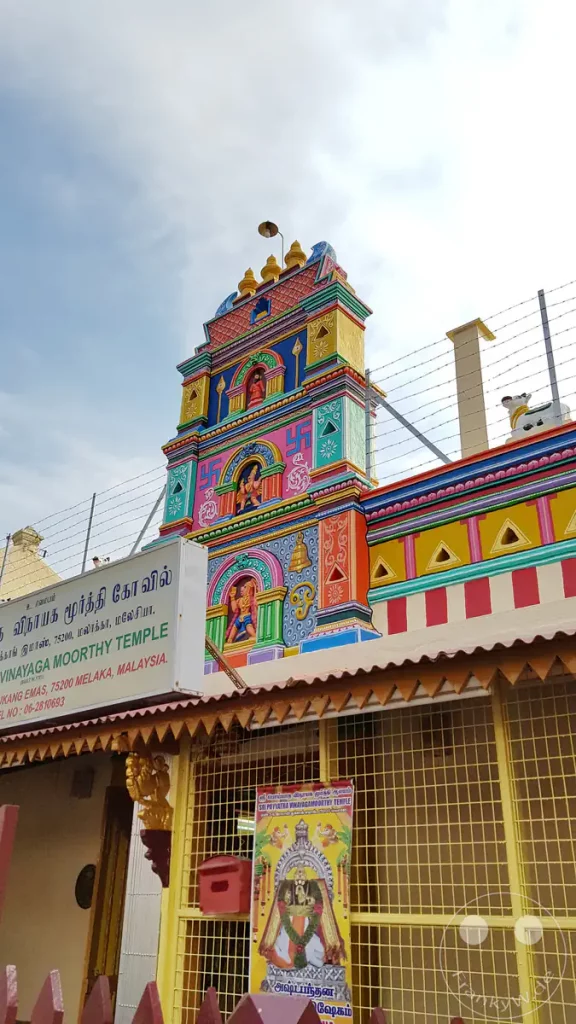Der farbenfroh gestaltete Eingangsturm des historischen Sri Poyatha Moorthi Tempels in der Stadt Melaka mit kunstvollen Verzierungen, Götterfiguren und bunten Bemalungen vor leicht bewölktem Himmel.