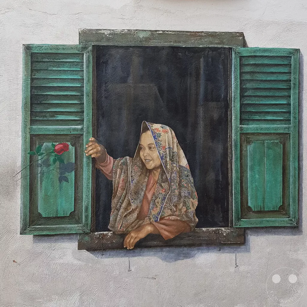 Ein dreidimensional wirkendes Wandgemälde in der Stadt Melaka, das eine lächelnde Frau mit Kopftuch zeigt, die aus einem geöffneten Holzfenster mit grünen Fensterläden blickt.