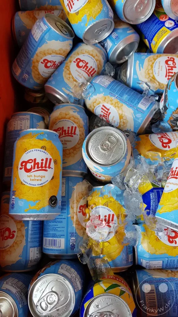 Viele hellblaue Getränkedosen der Marke Chill, darunter Sojamilch und Chrysanthemen-Tee, liegen gut gekühlt in Crushed Ice in einer roten Kühlbox an einer Raststätte bei Tangkak.