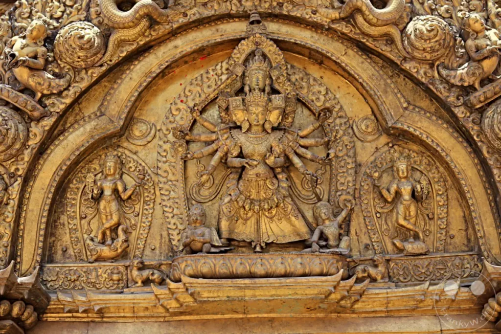 Eine detaillierte goldene Schnitzerei aus Bhaktapur, Nepal, zeigt eine zentrale mehrarmige Gottheit umgeben von weiteren Figuren. Das Kunstwerk besticht durch seine aufwendige Handwerkskunst und religiöse Symbolik.