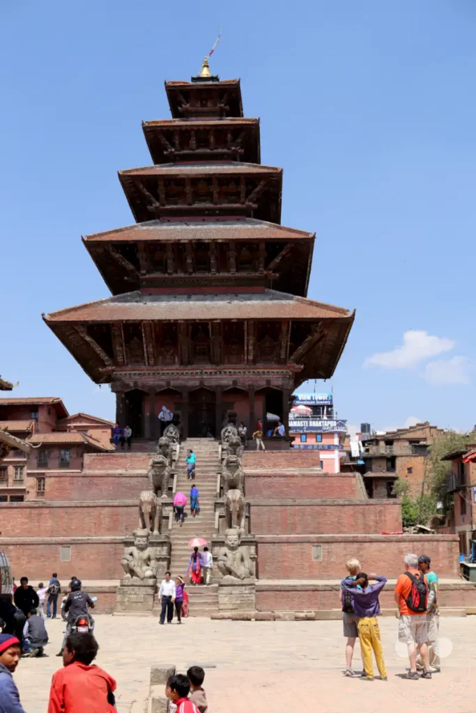 Der Nyatapola Tempel, ein fünfstöckiges Pagoden-Tempelgebäude, dominiert den Platz in Bhaktapur, Nepal. Touristen und Einheimische bewegen sich auf dem sonnigen Platz vor dem imposanten Backsteingebäude und den Stufen.
