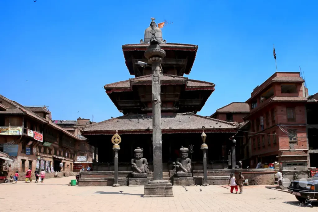Ein sonniger Tag auf dem historischen Tempelplatz von Bhaktapur, Nepal. Menschen schlendern durch die Gassen, während altehrwürdige Tempel und Gebäude die Szenerie dominieren. Die Atmosphäre ist ruhig und friedlich, geprägt von kultureller Bedeutung und lokaler Lebendigkeit.