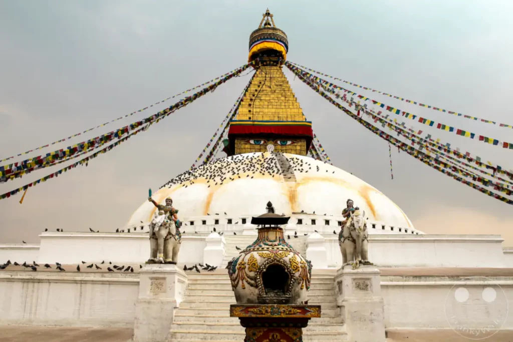 Der Boudhanath Stupa in Kathmandu ist ein UNESCO-Weltkulturerbe und einer der größten Stupas Nepals. Bunte Gebetsfahnen flattern im Wind und umgeben die kuppelförmige Struktur. Eine Vielzahl von Tauben hat sich auf der weißen Kuppel und den umliegenden Terrassen niedergelassen und verleiht der Szene eine lebendige Atmosphäre.