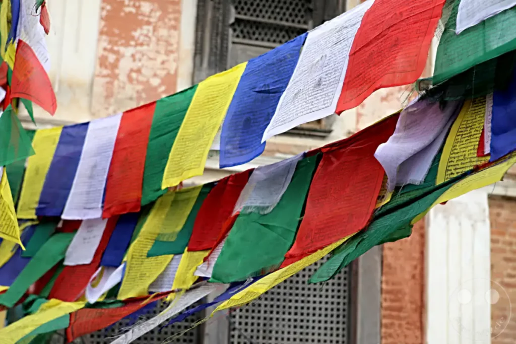 Bunte tibetische Gebetsfahnen flattern im Wind vor der Kulisse des Swayambhunath-Tempels in Kathmandu, Nepal. Die an Schnüren aufgehängten Stoffbahnen sind mit buddhistischen Gebeten und Symbolen bedruckt und vermitteln eine friedliche und spirituelle Atmosphäre.