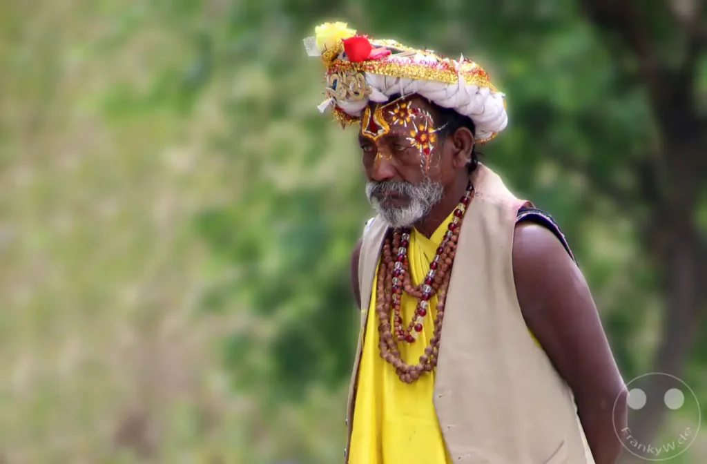 Ein Porträt eines Sadhu mit traditioneller Bemalung und Schmuck am Pashupatinath-Tempel in Kathmandu, Nepal. Die Aufnahme fängt die spirituelle Atmosphäre des Ortes während eines Festes ein.