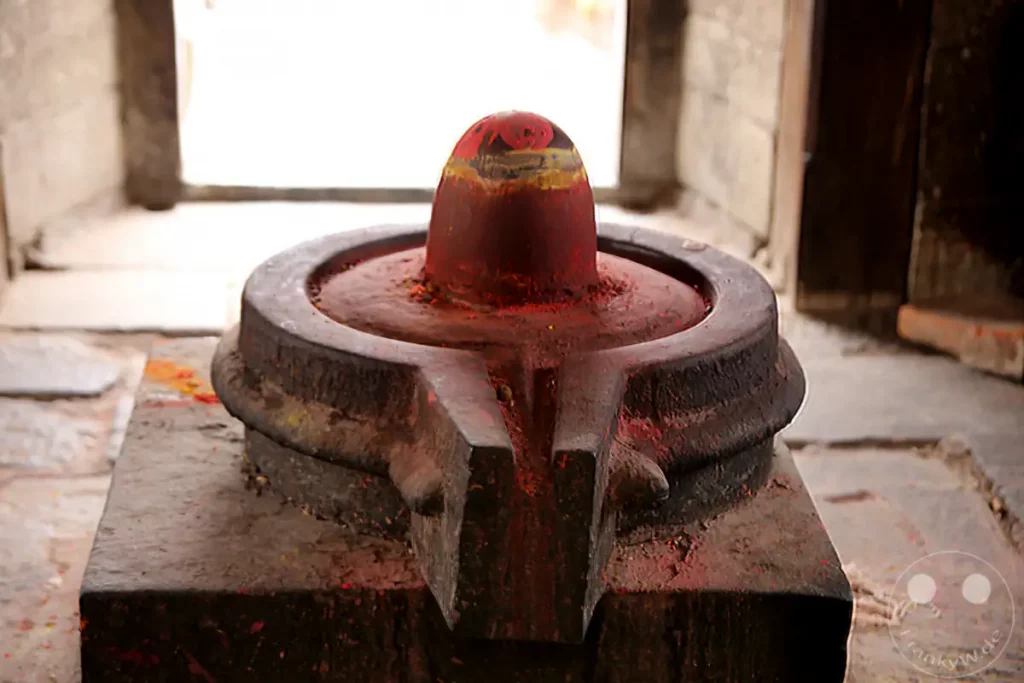 Ein Shiva Lingam, geschmückt mit roter Farbe und Pulver, steht auf einem steinernen Sockel im Pashupatinath-Tempel in Kathmandu, Nepal. Die Tempelanlage, ein wichtiger Hindu-Schrein, strahlt eine Atmosphäre tiefer Spiritualität und Hingabe aus.