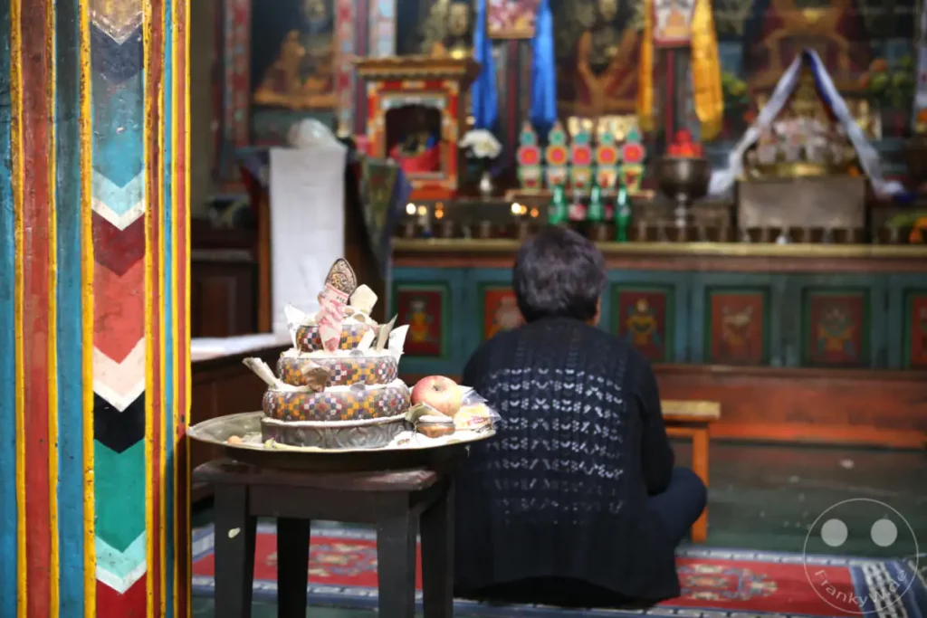 In der Swayambhunath-Stupa in Kathmandu, Nepal, werden Opfergaben vor einem buddhistischen Altar dargebracht. Eine Person sitzt im Hintergrund, beobachtet den Altarbereich und verweilt im spirituellen Ambiente des Tempels.