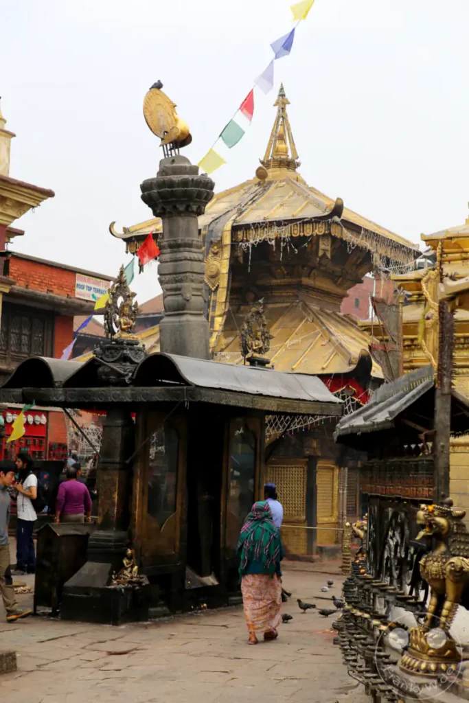 Die Swayambhunath-Stupa in Kathmandu, Nepal, ist ein bedeutender buddhistischer Tempelkomplex. Die Aufnahme zeigt goldene Dächer, kunstvolle Verzierungen, Gebetsfahnen und Gläubige, die den Ort besuchen. Die Atmosphäre ist geprägt von Spiritualität und kultureller Bedeutung.