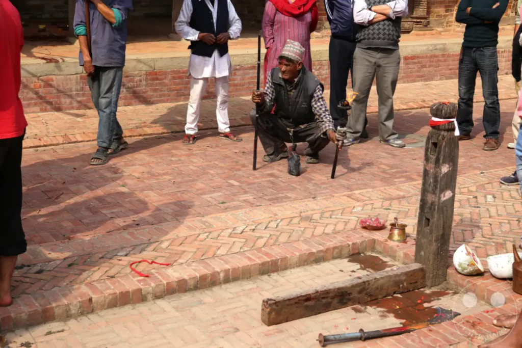 Auf dem Durbar Square in Patan, Nepal, versammeln sich Menschen um ein traditionelles Opferritual. Die Szene deutet auf eine religiöse Zeremonie in einem historischen Umfeld hin.