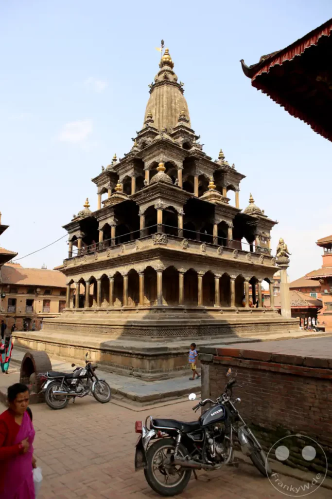 Der beeindruckende Nyatapola-Tempel im Durbar Square von Patan, Nepal, zeigt traditionelle nepalesische Architektur mit kunstvollen Schnitzereien und mehreren Ebenen. Die Szene ist belebt durch Einheimische und Besucher sowie geparkte Motorräder, was dem historischen Ort ein Gefühl von Alltagsleben verleiht.